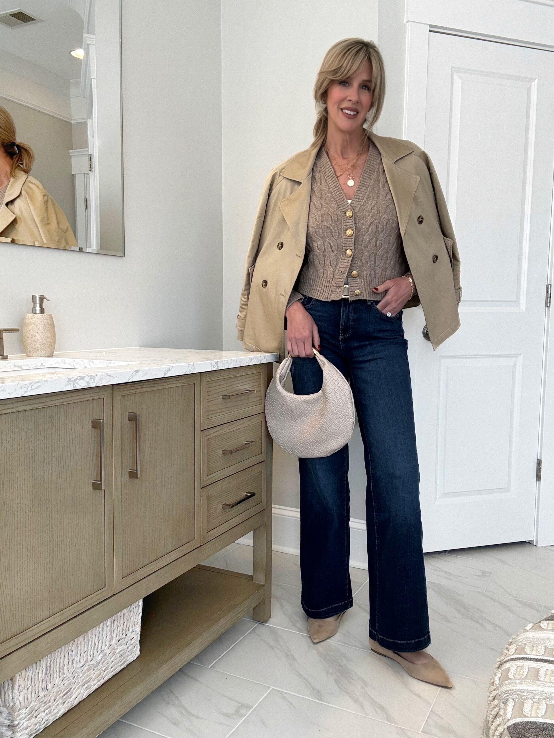 Woman sharing her everyday outfit inspiration wearing a cardigan sweater, cropped trench coat, wide leg denim with neutral accessories.